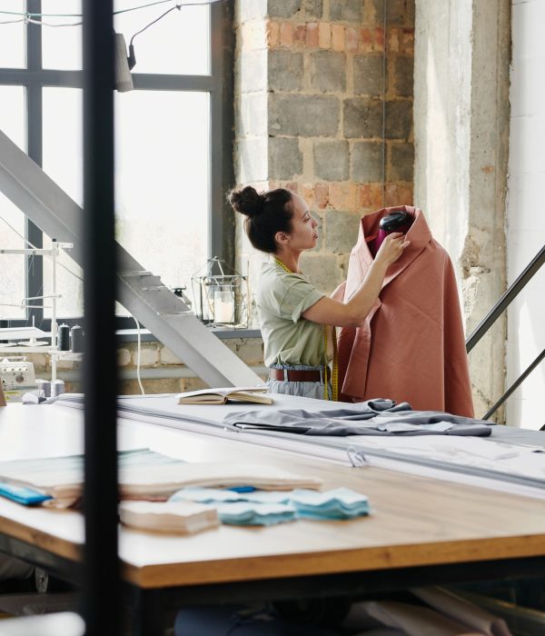 Female worker of modern fashion design studio sewing clothing item on dummy